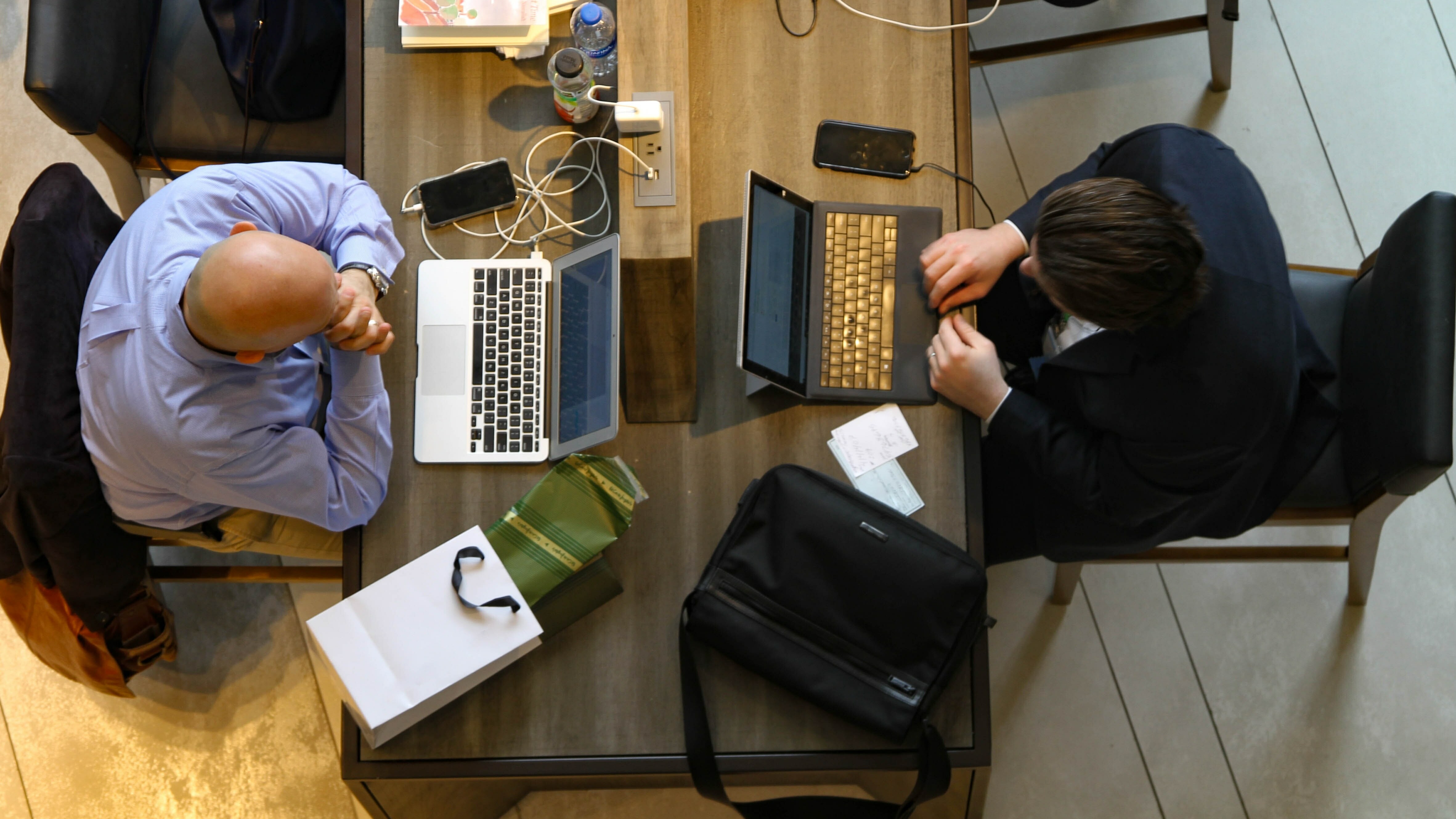 Zwei Männer von oben fotografiert. Sie sitzen sich an einem Tisch gegenüber und arbeiten an ihren Laptops.